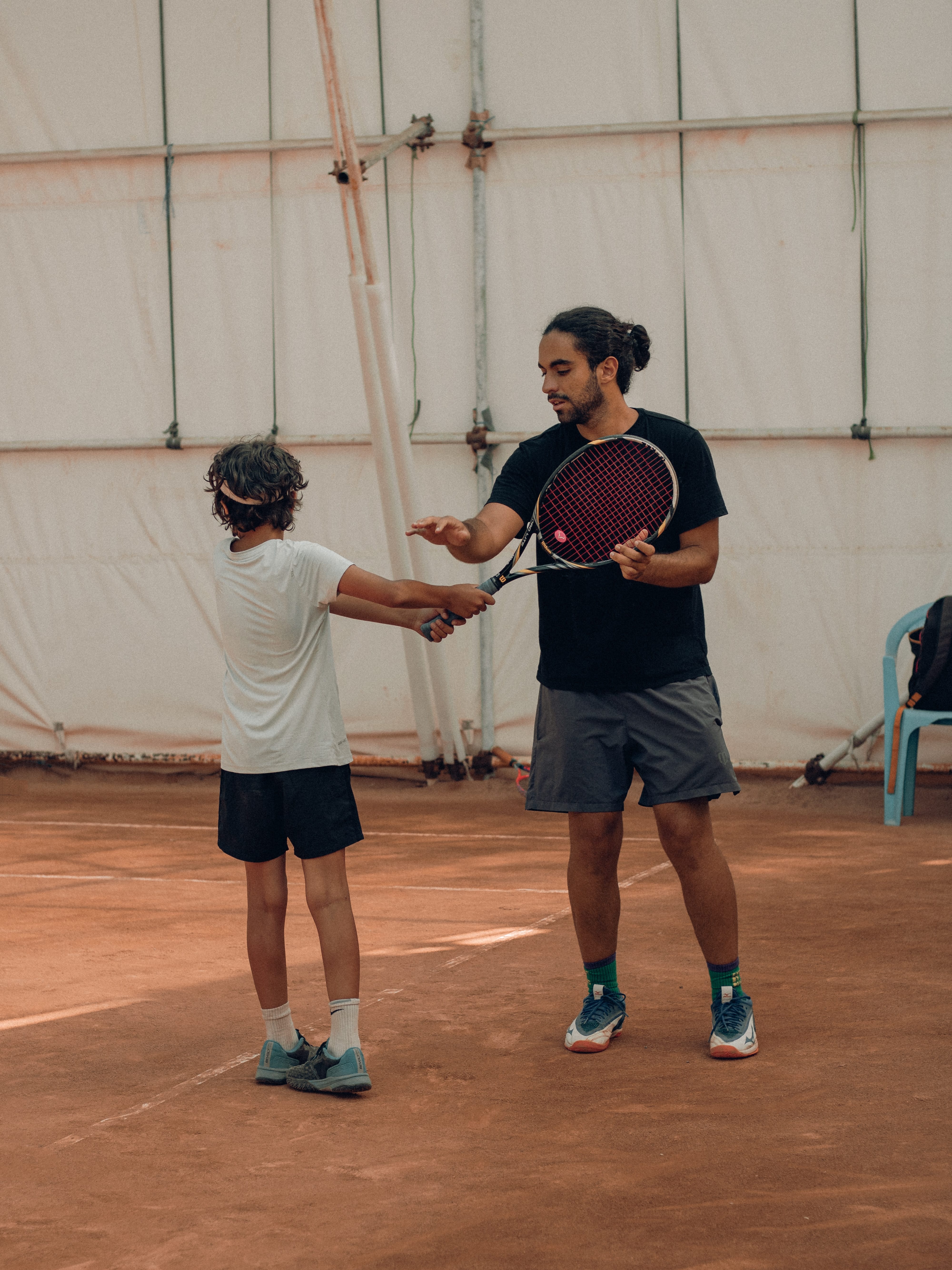 男性のテニスコーチが児童にテニスを指導する様子